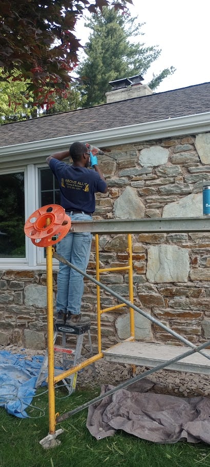 Team member on scaffold painting stone wall exterior of a house