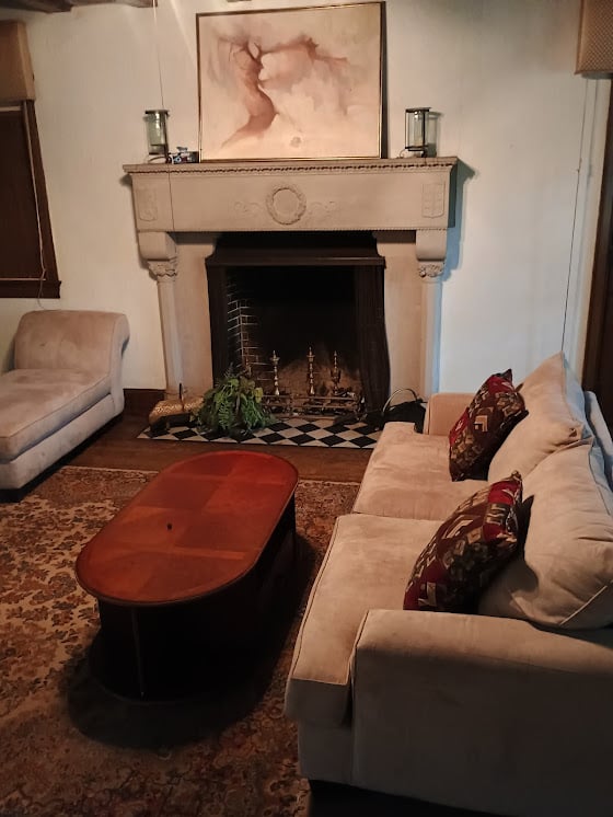 Cozy living room with a stone fireplace, beige sofas, an oval coffee table, and framed art above the mantel.