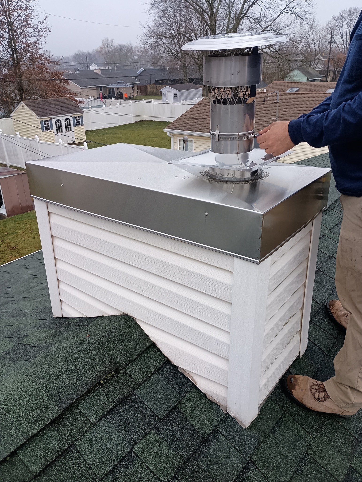 Team member adjusting a metal roof vent on a shingled rooftop