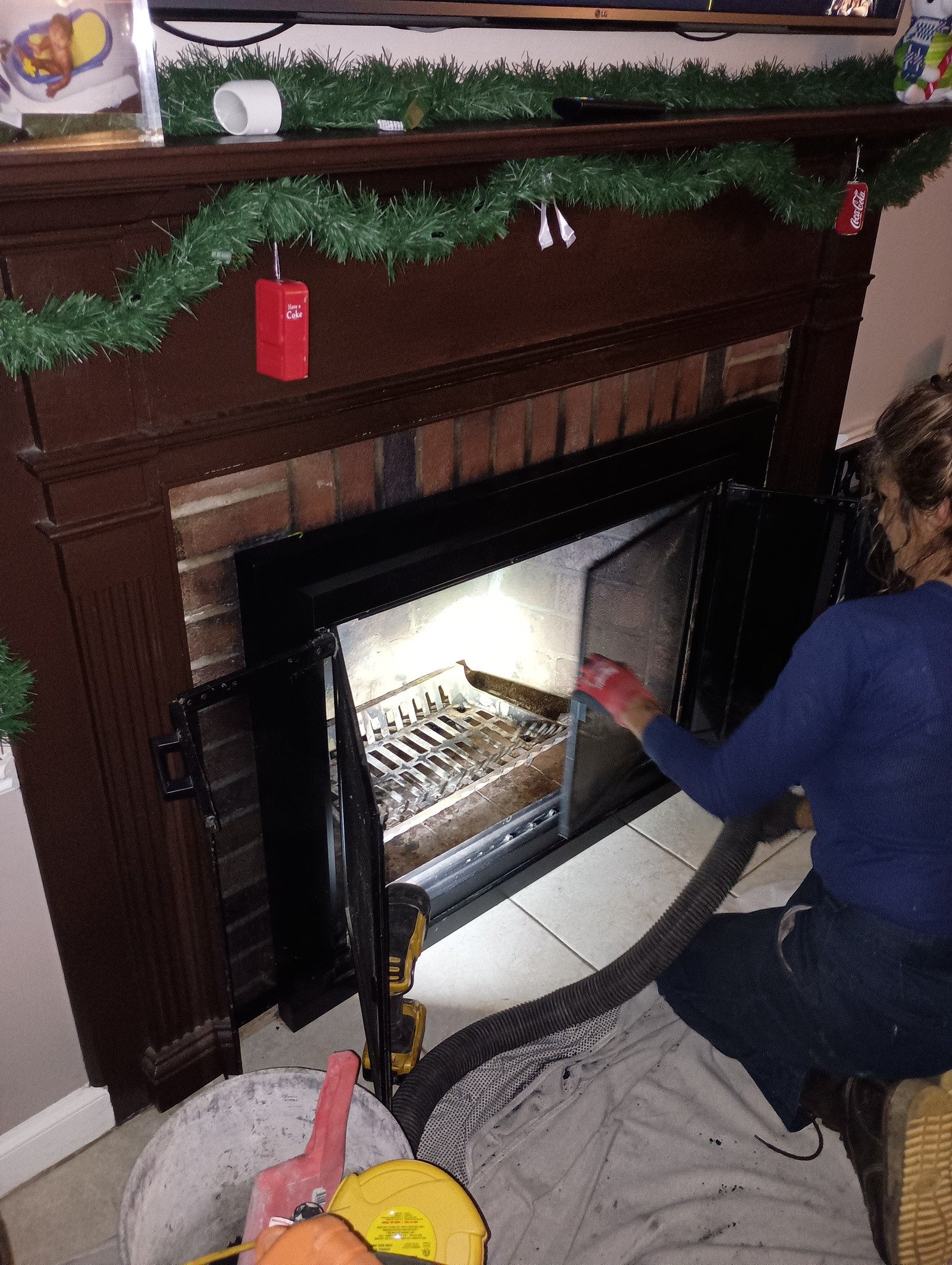 Team member cleaning an open fireplace with a vacuum hose, with holiday garland and Coca-Cola decorations on the mantel.