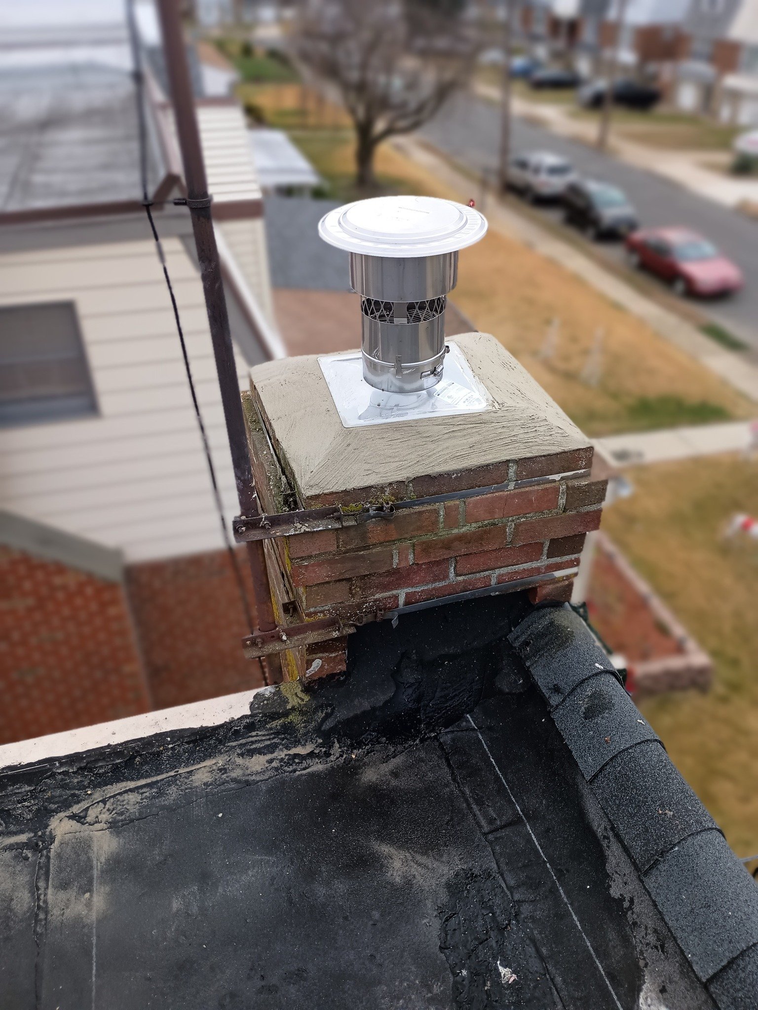 Rooftop chimney with a metal vent cap and surrounding black tar roof repair