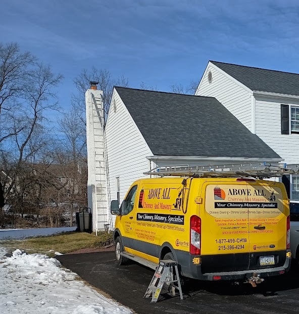 Above All Chimney & Masonry van parked by a white house with a ladder on the roof.