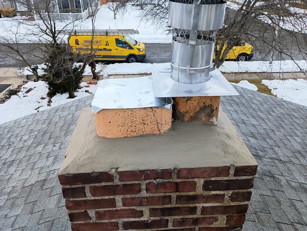 Snowy rooftop with a brick chimney, metal flue, and yellow service vans on the street below